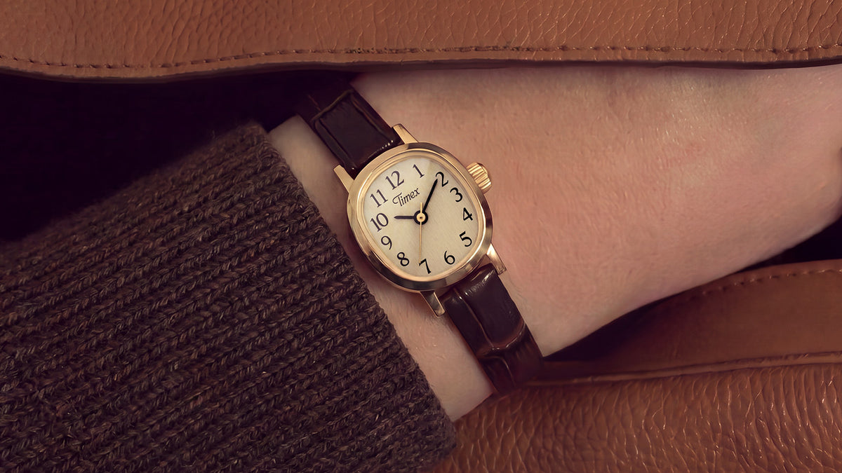 Reloj Cavatina® Mini con correa de piel marrón oscuro, que se lleva en la muñeca bajo la manga de un abrigo marrón.