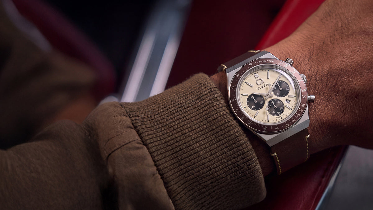 Q Timex Chronograph with a cream dial and brown leather strap styled on the wrist inside a red car interior.