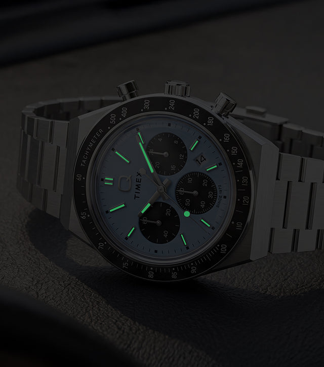 Q Timex Chronograph in low light, highlighting its glowing hands and hour markers.