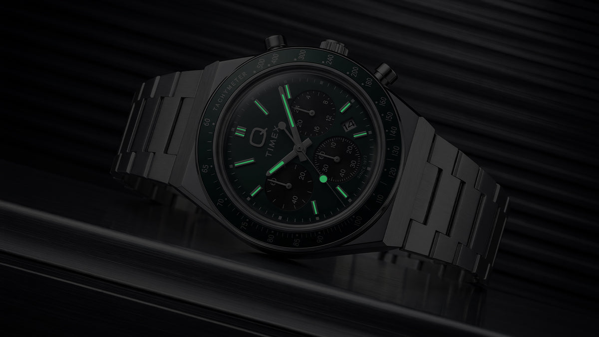 Q Timex Chronograph in darkness with illuminated hands and hour markers.