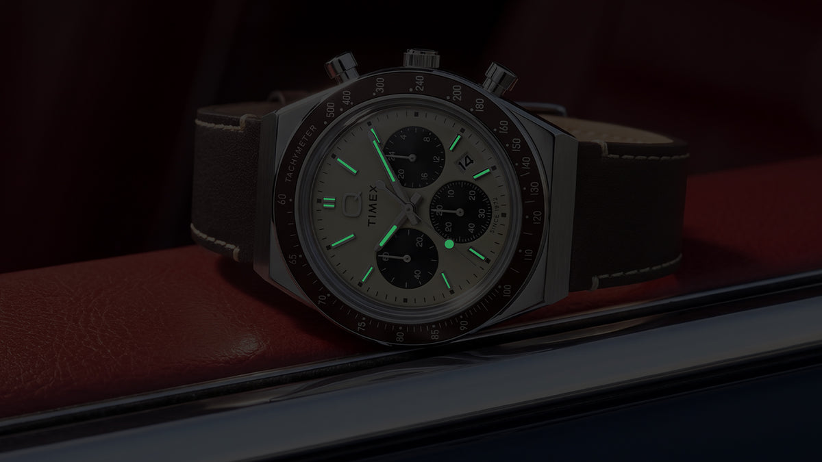 Q Timex Chronograph in darkness with illuminated hands and hour markers.