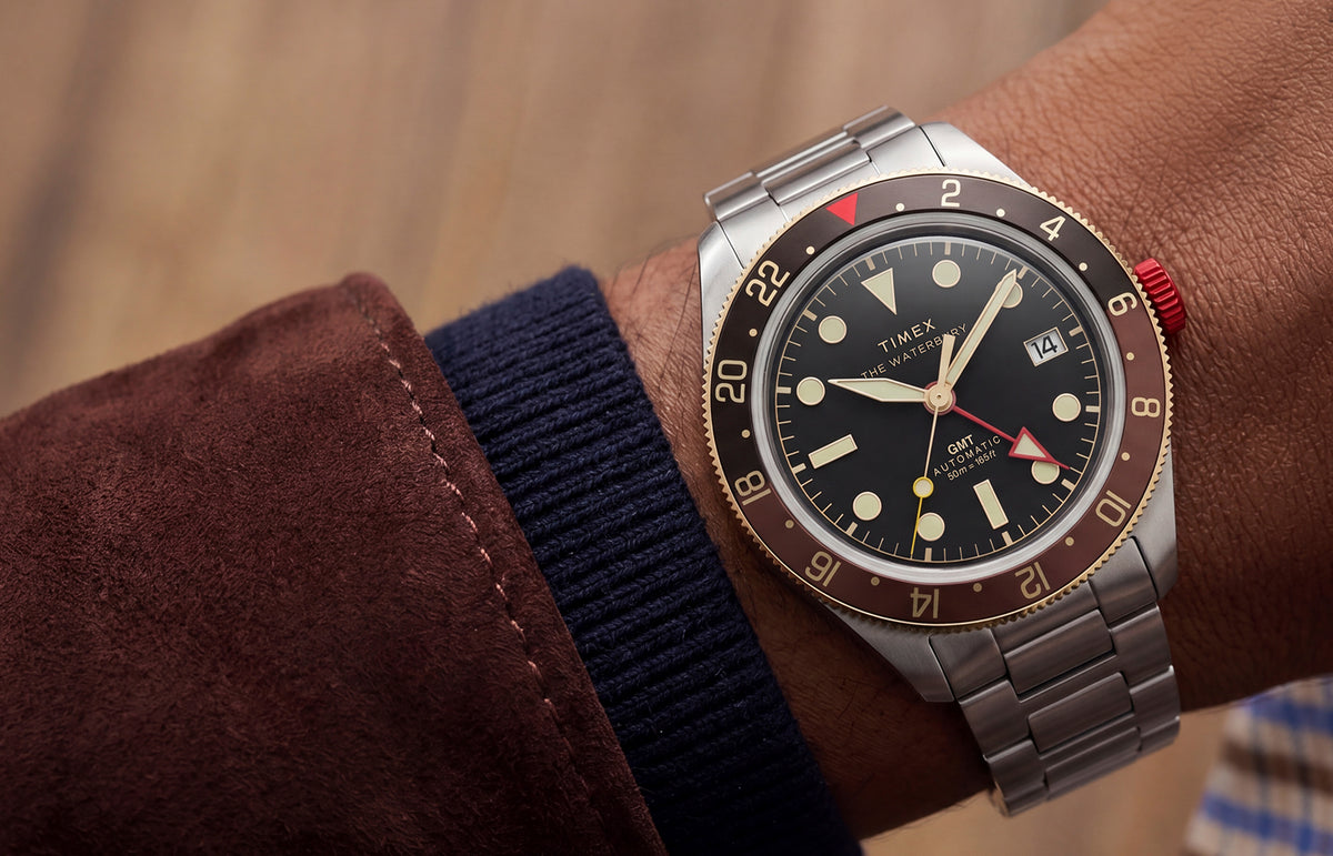 Close-up of the Waterbury Heritage Automatic GMT watch worn on the wrist with layered brown and navy sleeves.