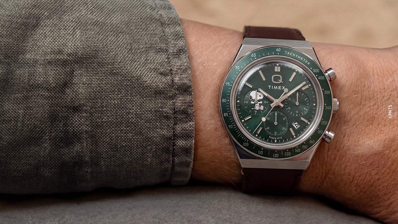 Cronógrafo Peanuts® x Q Timex con esfera verde y correa de piel marrón, puesto en la muñeca.