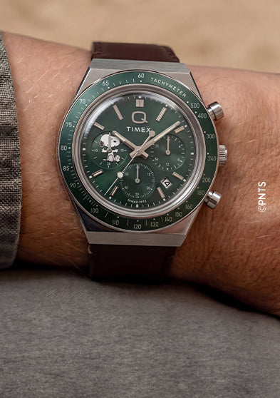 Cronógrafo Peanuts® x Q Timex con esfera verde y correa de piel marrón, puesto en la muñeca.
