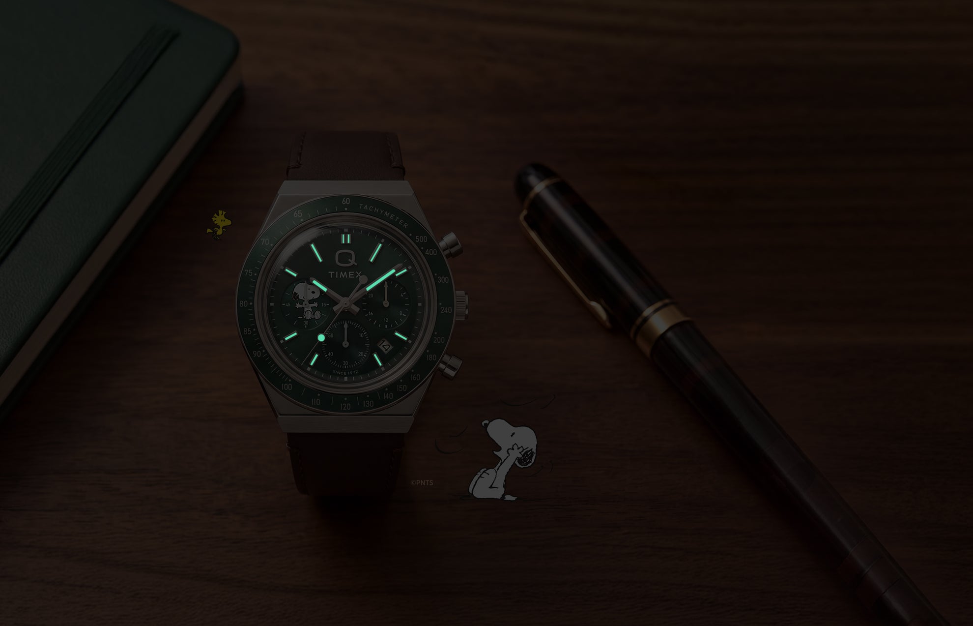 Cronógrafo Peanuts® x Q Timex, mostrado en condiciones de poca luz con agujas e índices luminosos.
