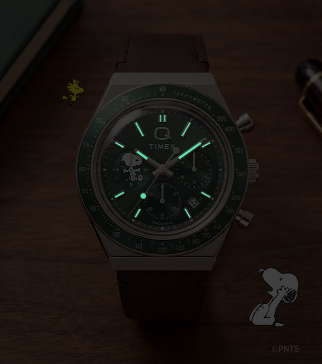 Cronógrafo Peanuts® x Q Timex, mostrado en condiciones de poca luz con agujas e índices luminosos.