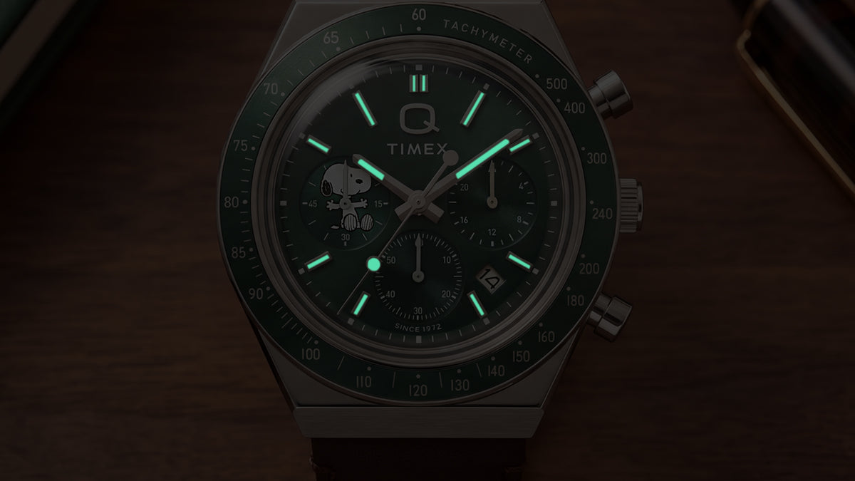 Primer plano de la esfera del cronógrafo Peanuts® x Q Timex con poca luz, en el que destacan sus agujas e índices luminosos.
