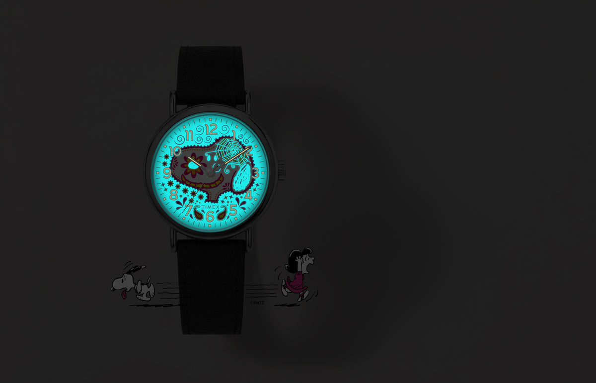 Peanuts® x Timex Weekender® Day of the Dead watch shown in the dark with its blue INDIGLO® dial illuminating the Snoopy sugar-skull design.