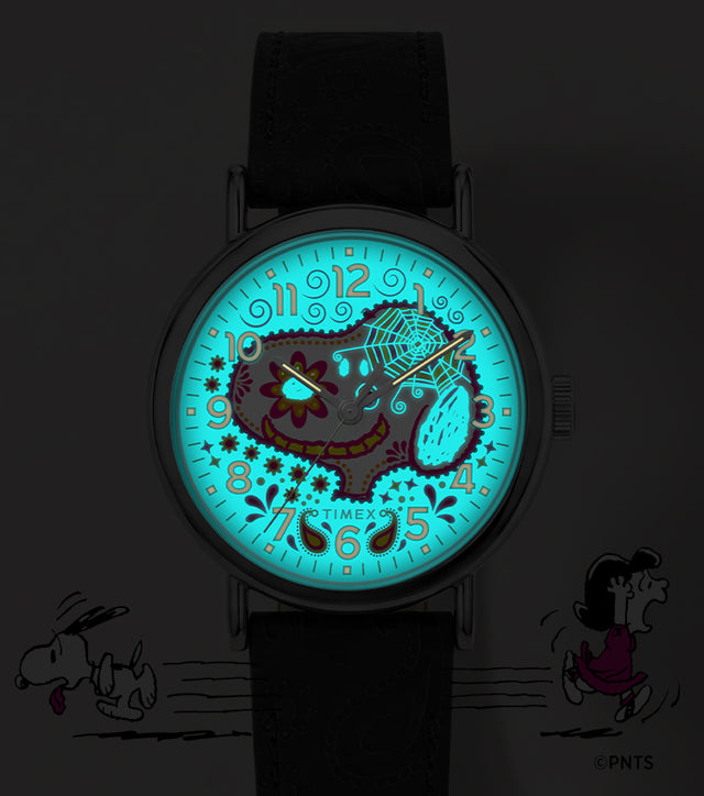 Peanuts® x Timex Weekender® Day of the Dead watch shown in the dark with its blue INDIGLO® dial illuminating the Snoopy sugar-skull design.
