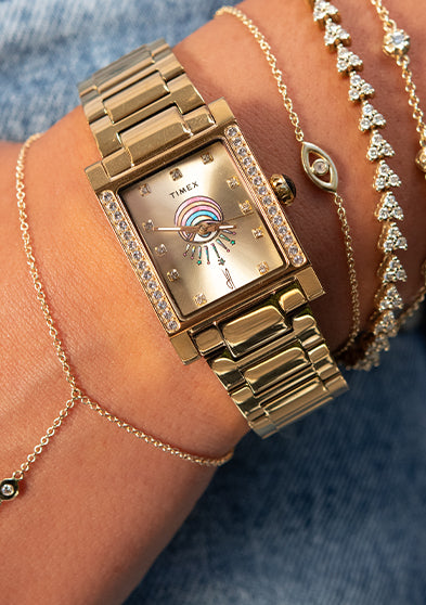 Gold-tone Timex x Jacquie Aiche Éclat watch worn with layered gold and crystal bracelets.