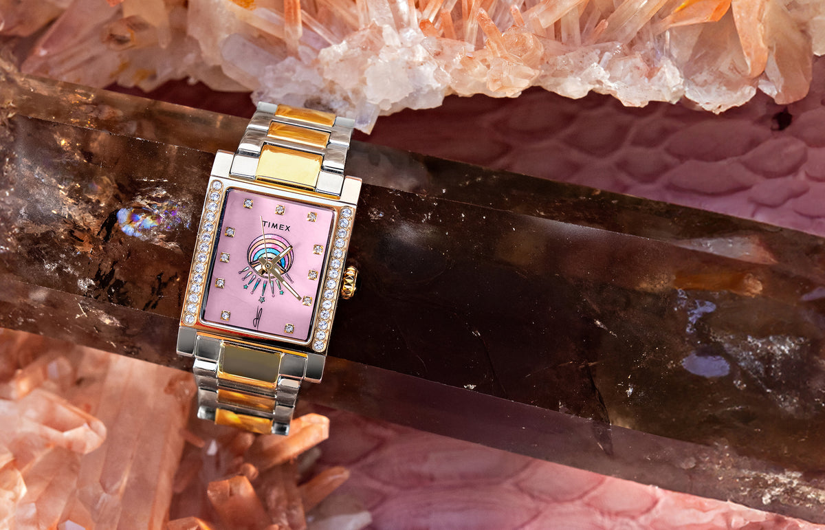 Timex x Jacquie Aiche Éclat two-tone watch with a pink dial, crystal accents, and eye motif among pink crystals.