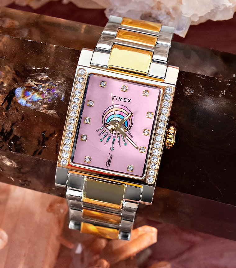 Timex x Jacquie Aiche Éclat two-tone watch with a pink dial, crystal accents, and eye motif among pink crystals.