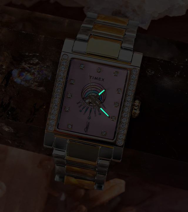 Timex x Jacquie Aiche Éclat watch in low light, revealing glowing hands against its pink dial.