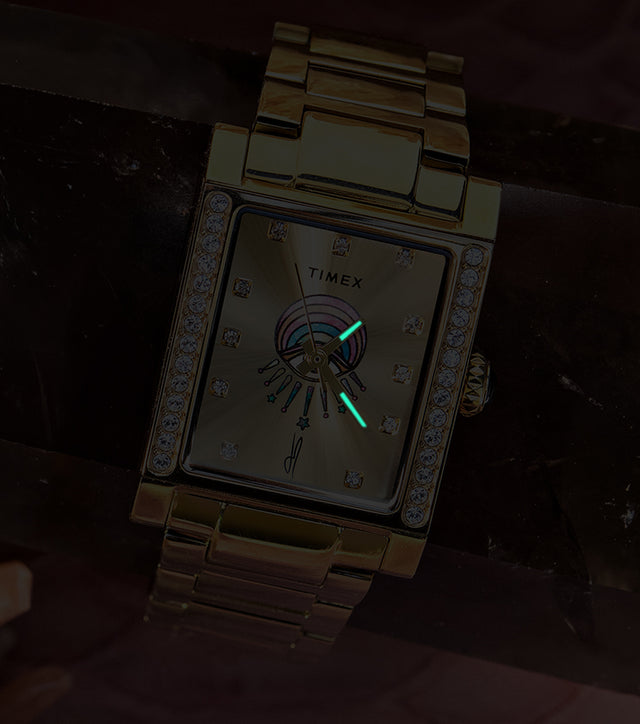Gold-tone Timex x Jacquie Aiche Éclat watch in low light, showing glowing hands against its champagne dial.