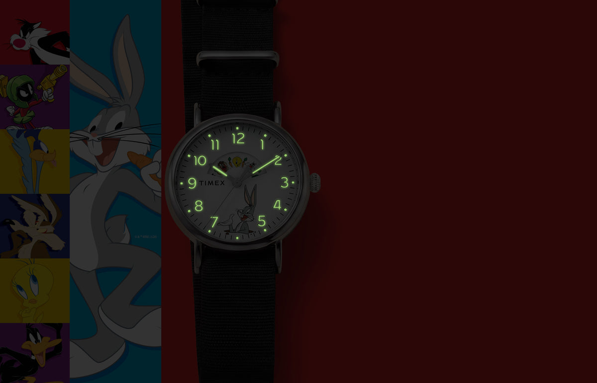 TW2Y99100 Looney Tunes Bugs and Friends x Timex Standard watch with glowing green hands and numerals beside Looney Tunes character artwork.