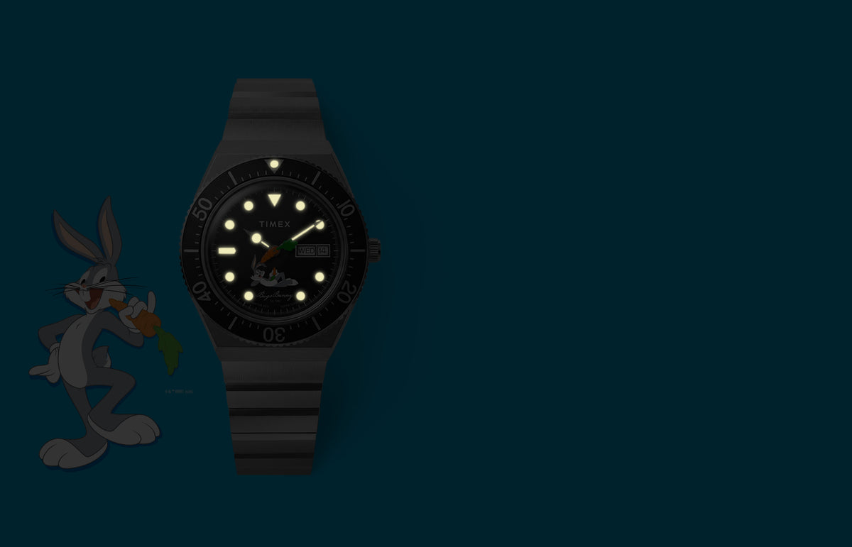 TW2Y99200 Bugs Bunny x Timex M79 watch with glowing hands and hour markers beside Bugs Bunny artwork in dim lighting.