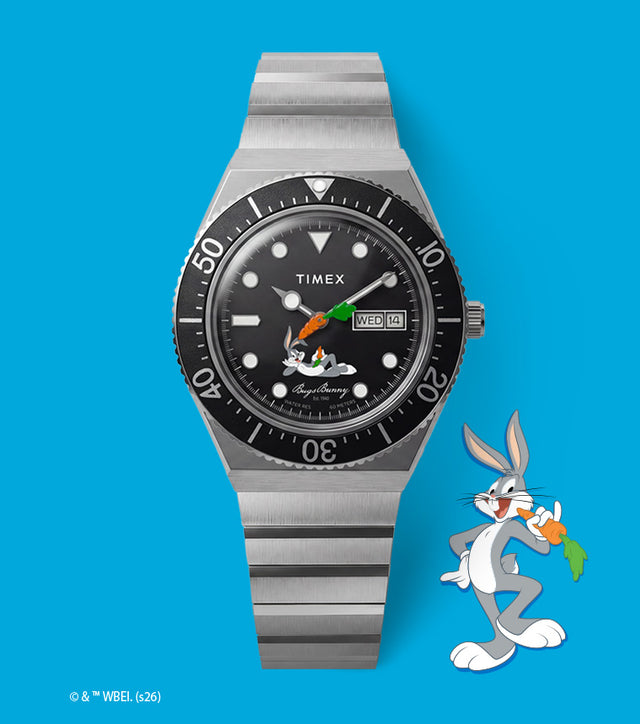 TW2Y99200 Looney Tunes Bugs Bunny x Timex M79 Automatic Signature Edition watch with a black dial and silver-tone bracelet beside Bugs Bunny artwork on blue.