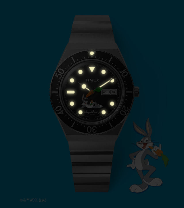 TW2Y99200 Bugs Bunny x Timex M79 watch with glowing hands and hour markers beside Bugs Bunny artwork in dim lighting.
