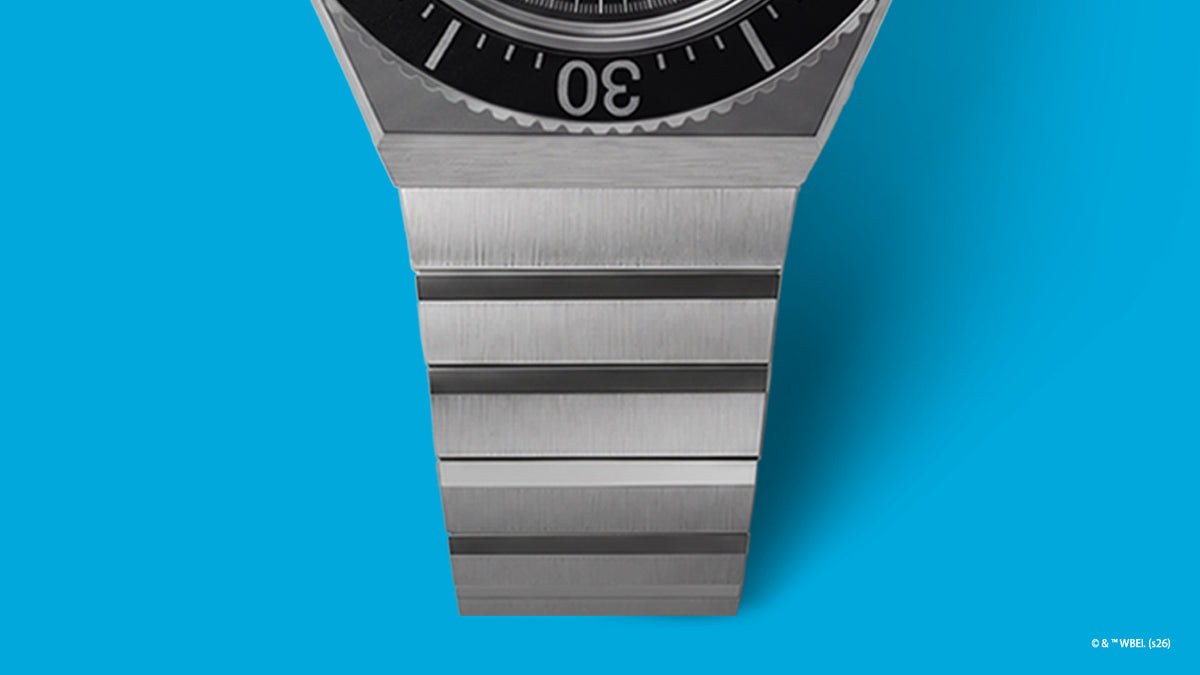 TW2Y99200 Close-up of the brushed silver-tone bracelet and black bezel on the Bugs Bunny x Timex M79 watch against blue.