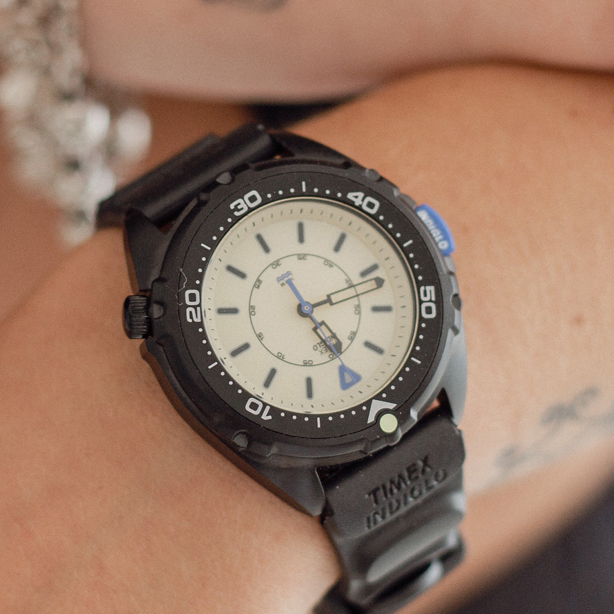 TW6A19800 Close-up of the Timex Intrepid x Dimepiece ‘Blackout’ Edition on a wrist, showing its cream dial, black bezel and blue accents.
