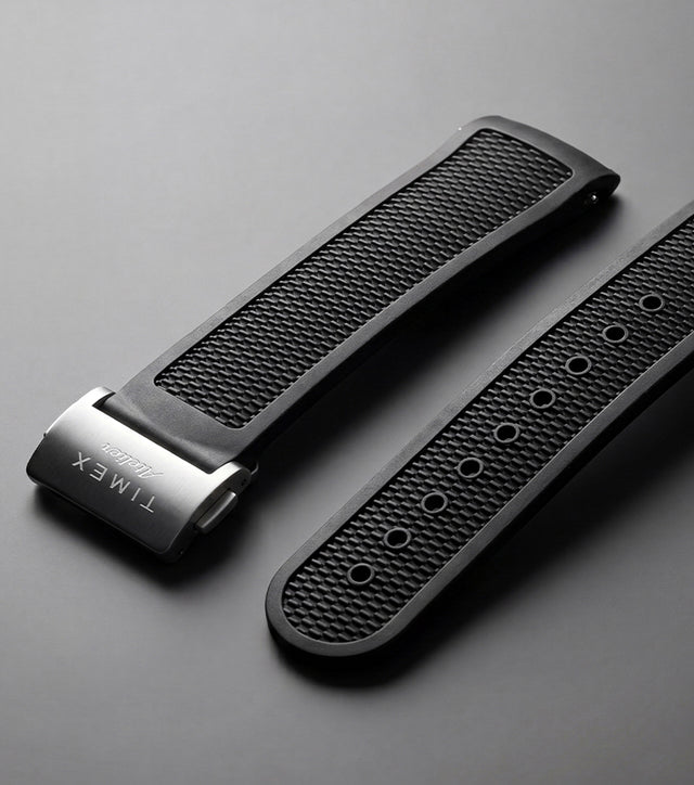 Timex Atelier NBR synthetic rubber strap in black with a textured finish and stainless-steel clasp, displayed against a dark background.
