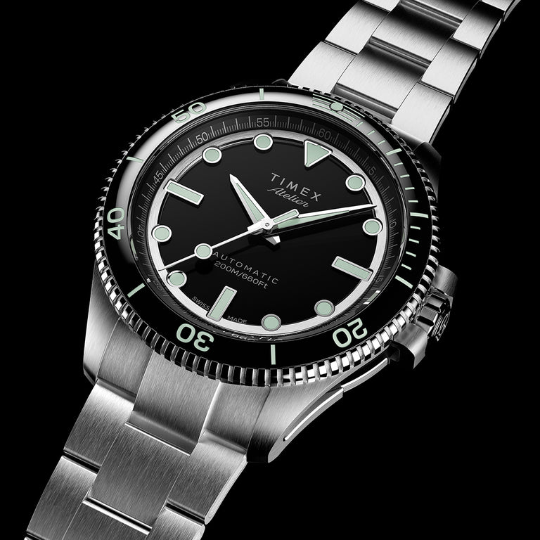 Reloj de buceo automático Timex Atelier con esfera negra, índices luminosos, bisel giratorio y brazalete de acero inoxidable.