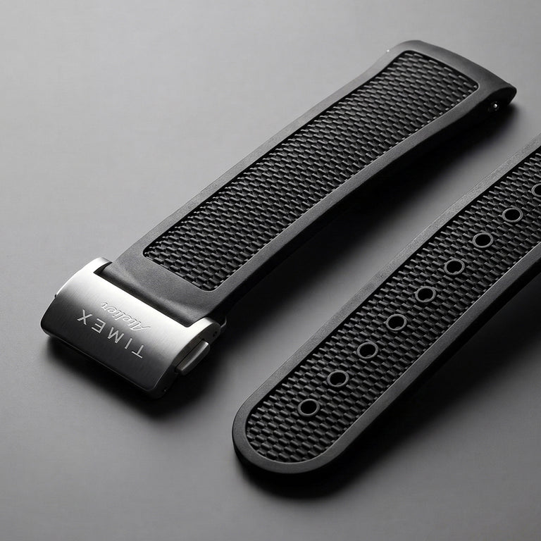 Dos correas de reloj de caucho negro texturizado con un cierre Timex Atelier de acero inoxidable cepillado.
