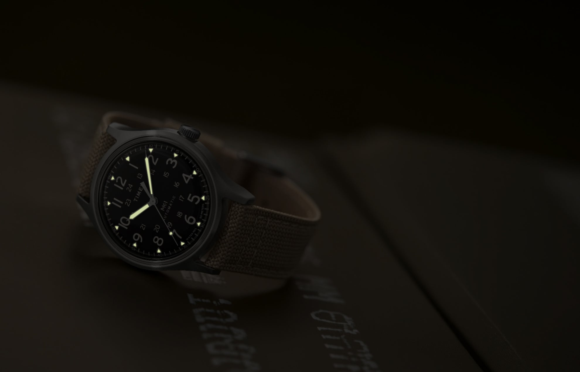 MK1® Automatic watch in low light, highlighting its glowing hands and hour markers.