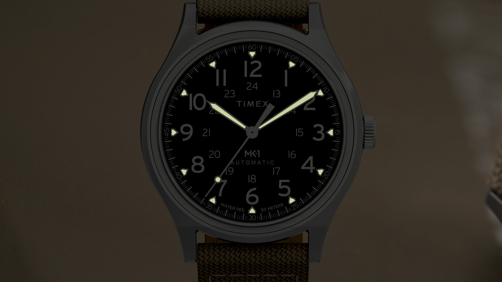 Front view of the MK1® Automatic watch in low light, showing its luminous hands and hour markers.