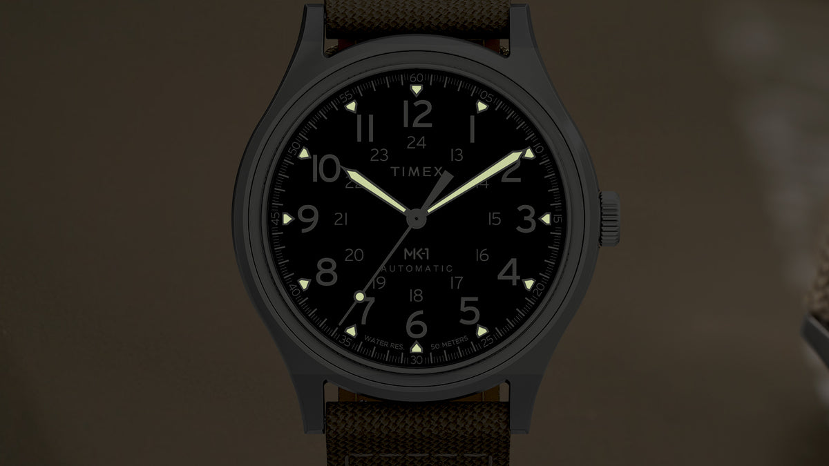 Front view of the MK1® Automatic watch in low light, showcasing its luminous hands and hour markers.