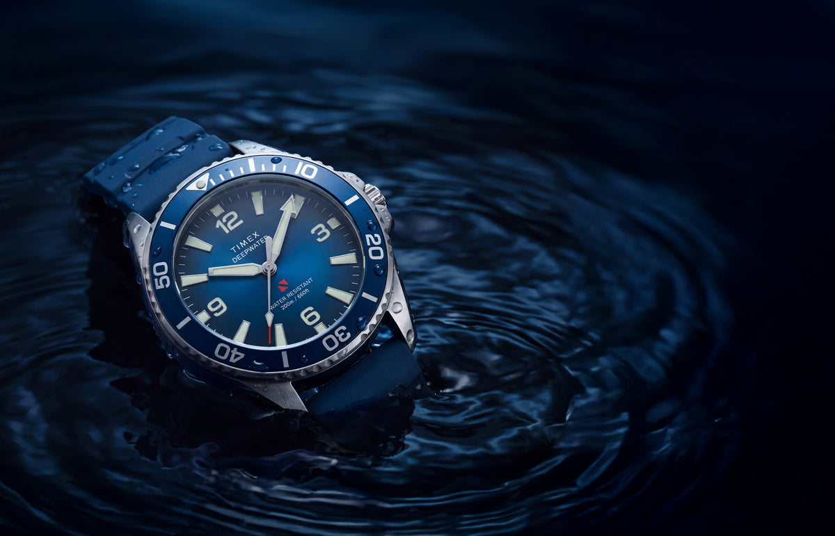 TW3A01900 Deepwater Arctic 200 watch with a blue dial and strap resting in dark, rippling water.