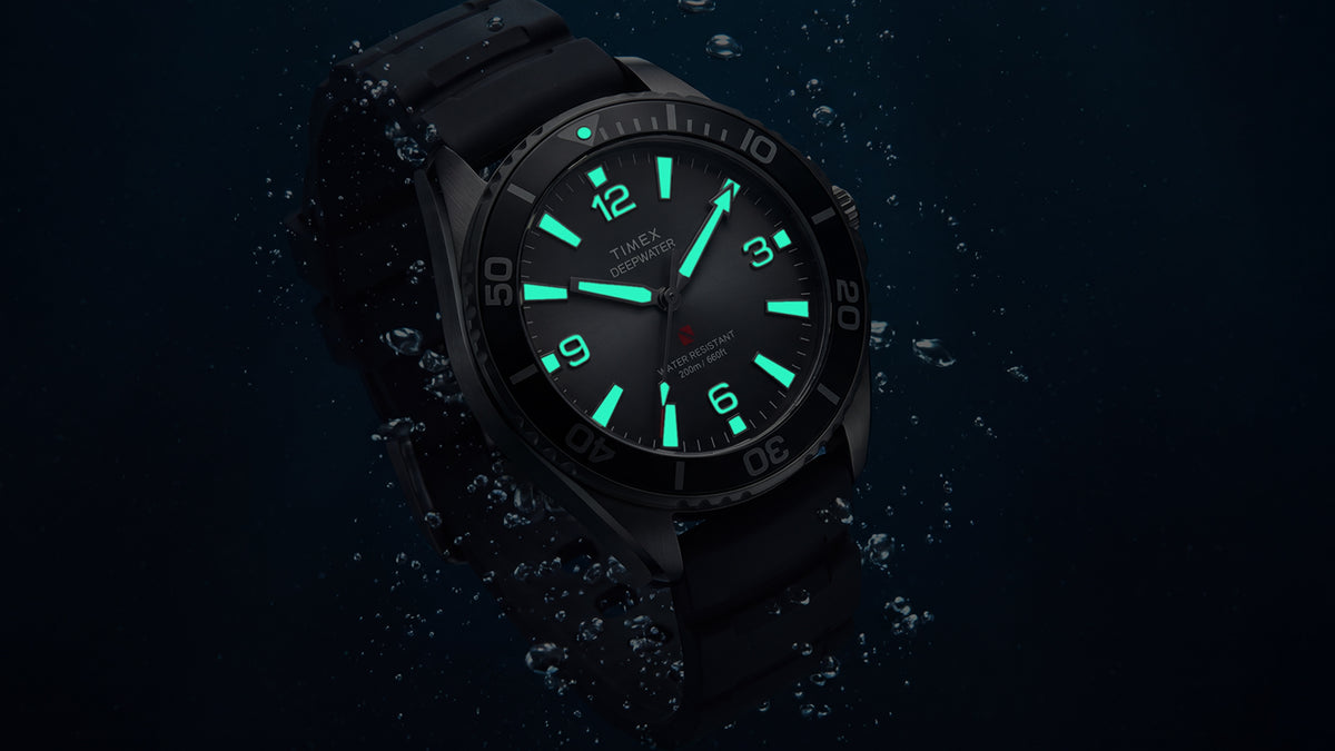 TW3A02000 Angled view of the Deepwater Arctic 200 watch with glowing aqua hands and hour markers amid underwater bubbles.