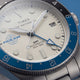 TW2Y94300 Macro view of the cream dial with the Pan Am logo, blue GMT hand, date window, and blue-and-black bezel.