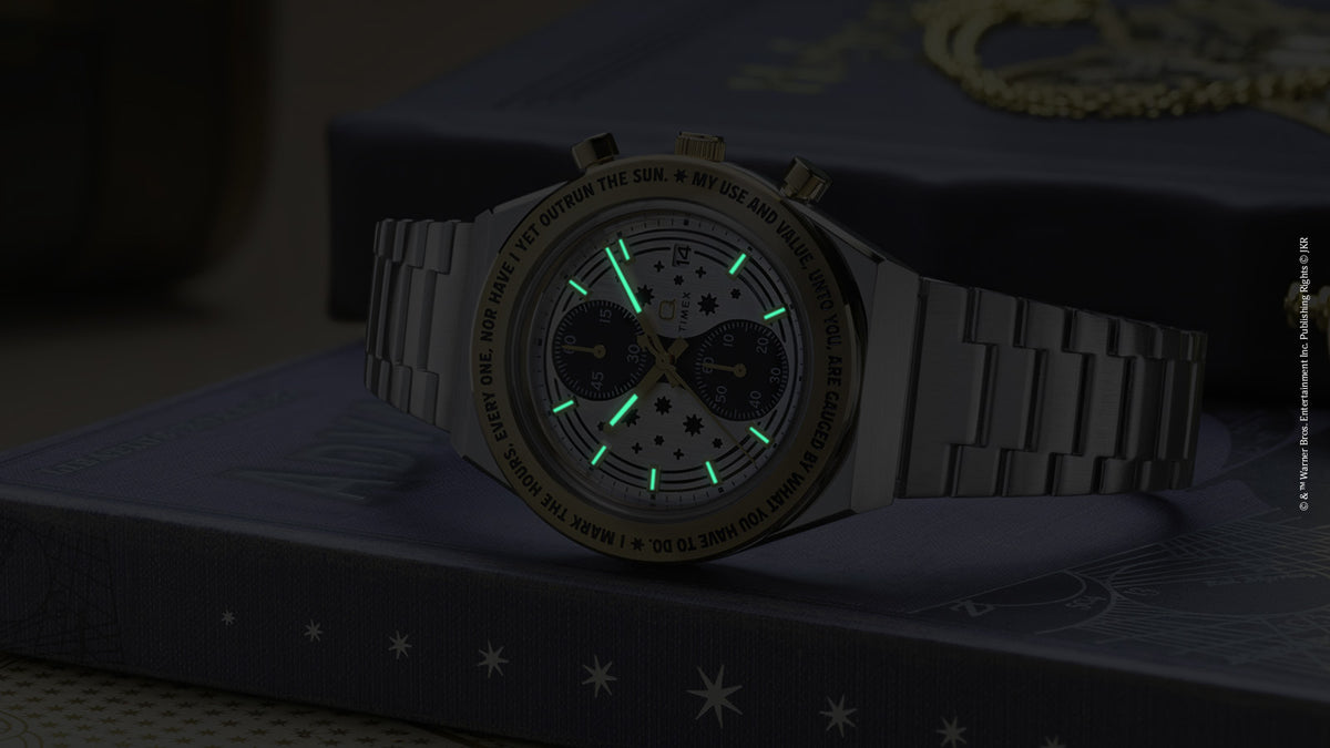 TW2Y75900 The watch displayed on a book in dim light, with its hands and hour markers glowing green.
