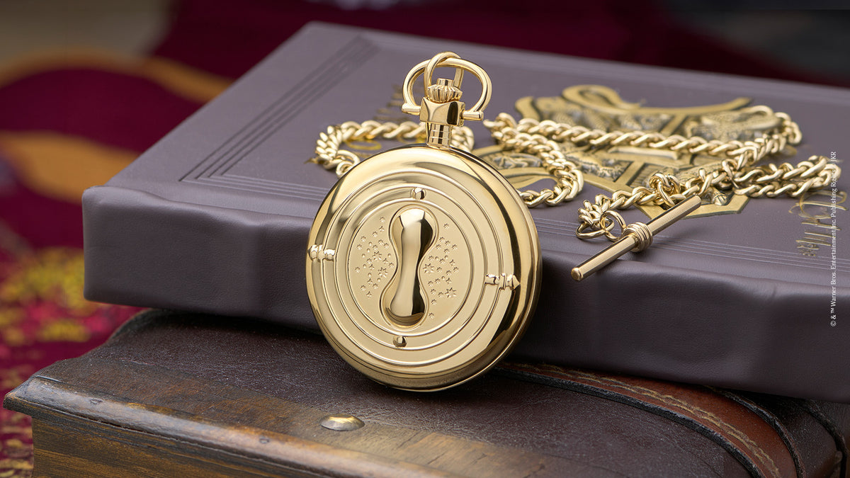 TW2Y99600 Back of the gold-tone pocket watch, featuring an hourglass design, with its chain resting on a book.