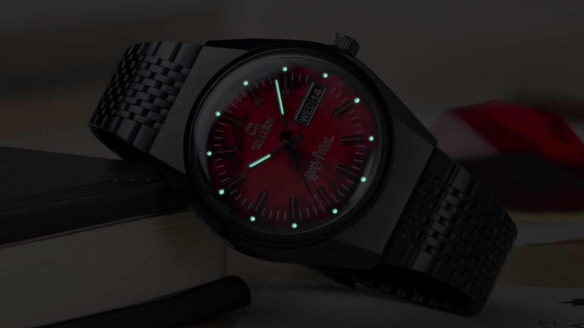 TW2Y99700 Harry Potter x Q Timex watch shown in darkness with luminous green hands and hour markers glowing against the red dial.