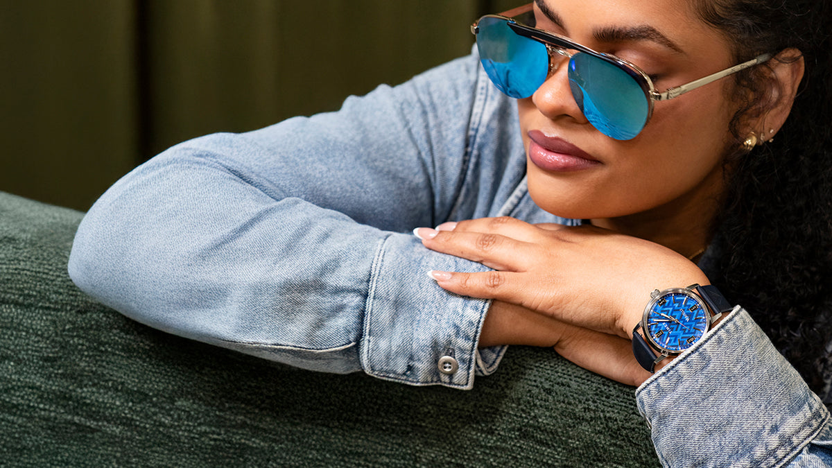 TW2Y73800 Woman in blue sunglasses wearing the blue-dial watch while resting her arms on a green chair.