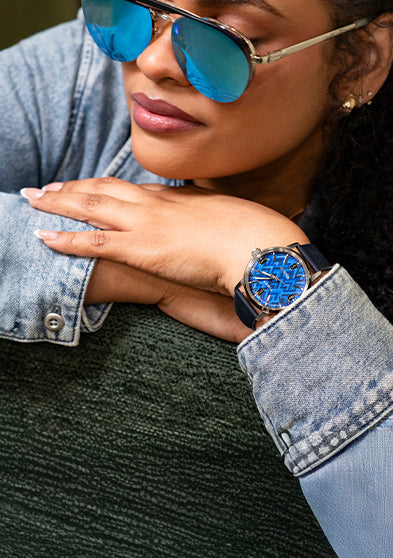 TW2Y73800 Woman in blue sunglasses wearing the blue-dial watch while resting her arms on a green chair.