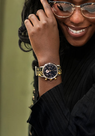 TWG069100: Mujer sonriente con gafas y un reloj de esfera negra con correa estampada en negro y dorado.