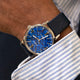 TW2Y73800 Close-up of the blue-dial watch worn with a striped shirt and dark jacket.