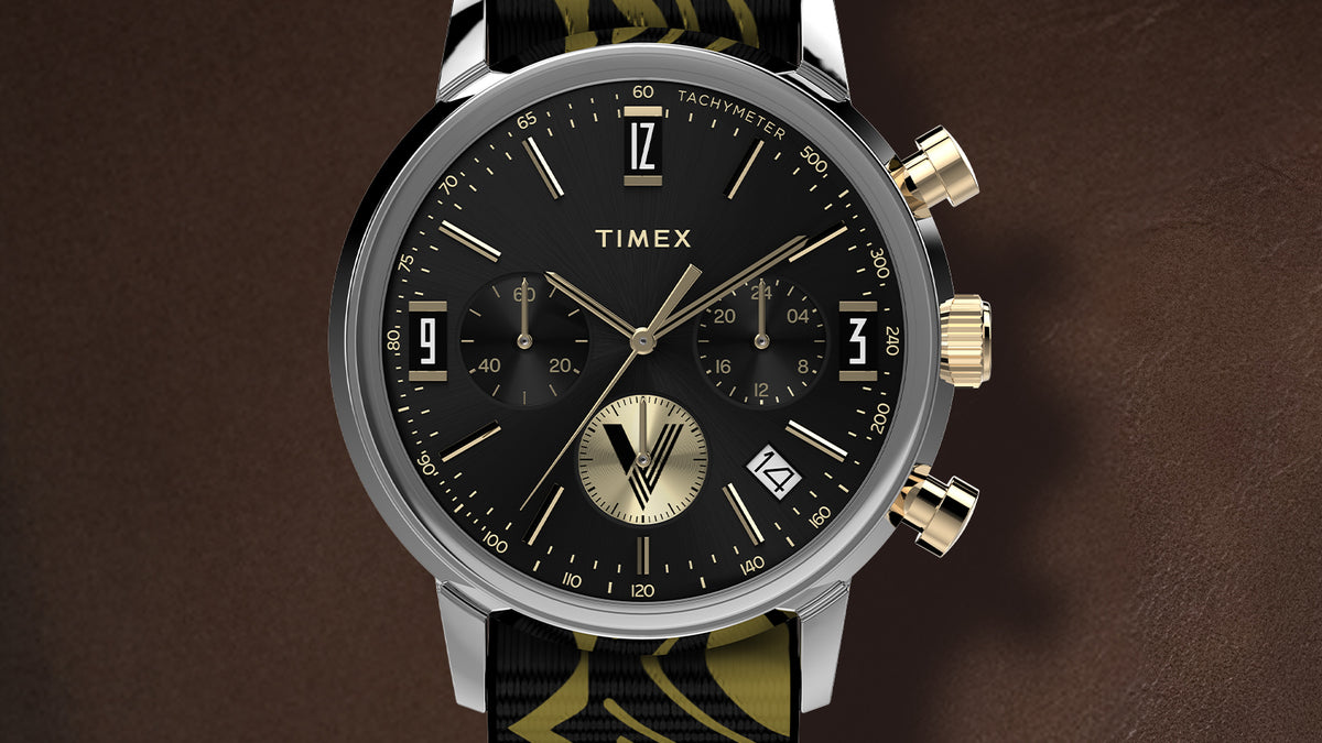 TWG069100 Primer plano de la esfera negra del cronógrafo del reloj, con agujas y detalles en tono dorado, y ventana de fecha.