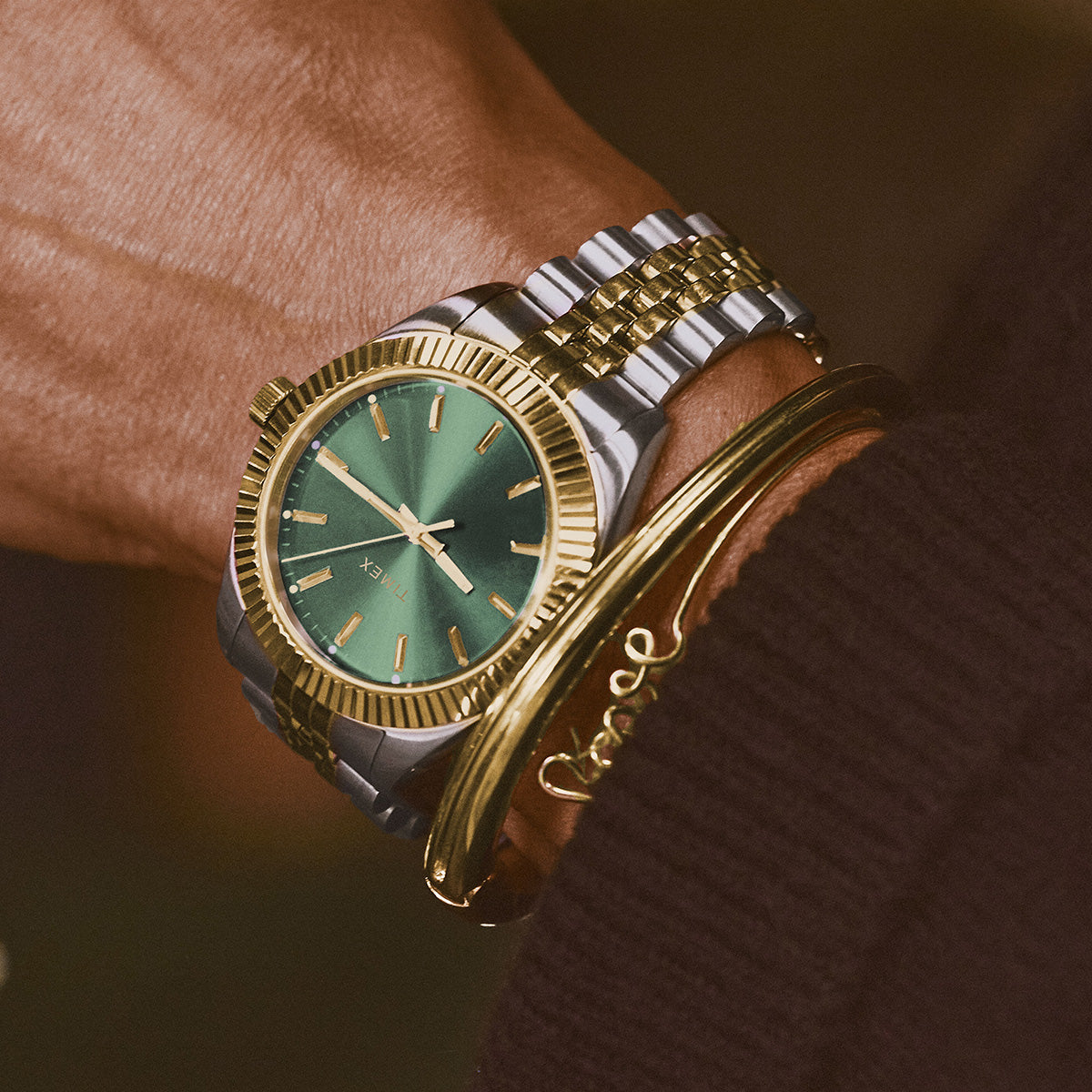 Reloj Timex bicolor con esfera verde, combinado con pulseras doradas.