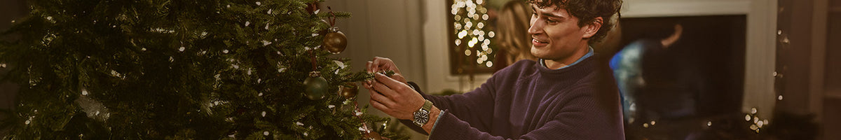 Regalos para él: un hombre que lleva un reloj Timex con correa verde mientras decora un árbol de Navidad.