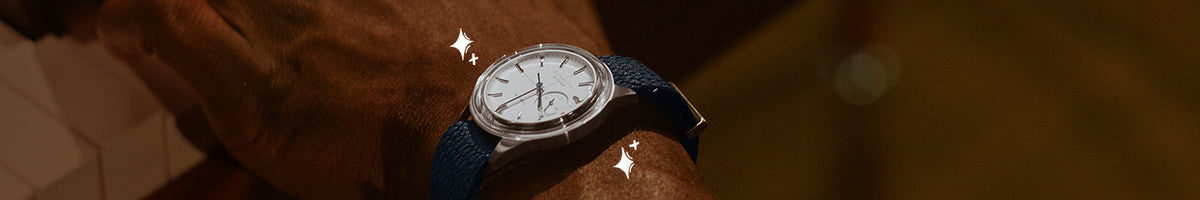 Regalos de lujo: primer plano de un reloj Timex con esfera blanca, caja plateada y correa azul marino, puesto en la muñeca.