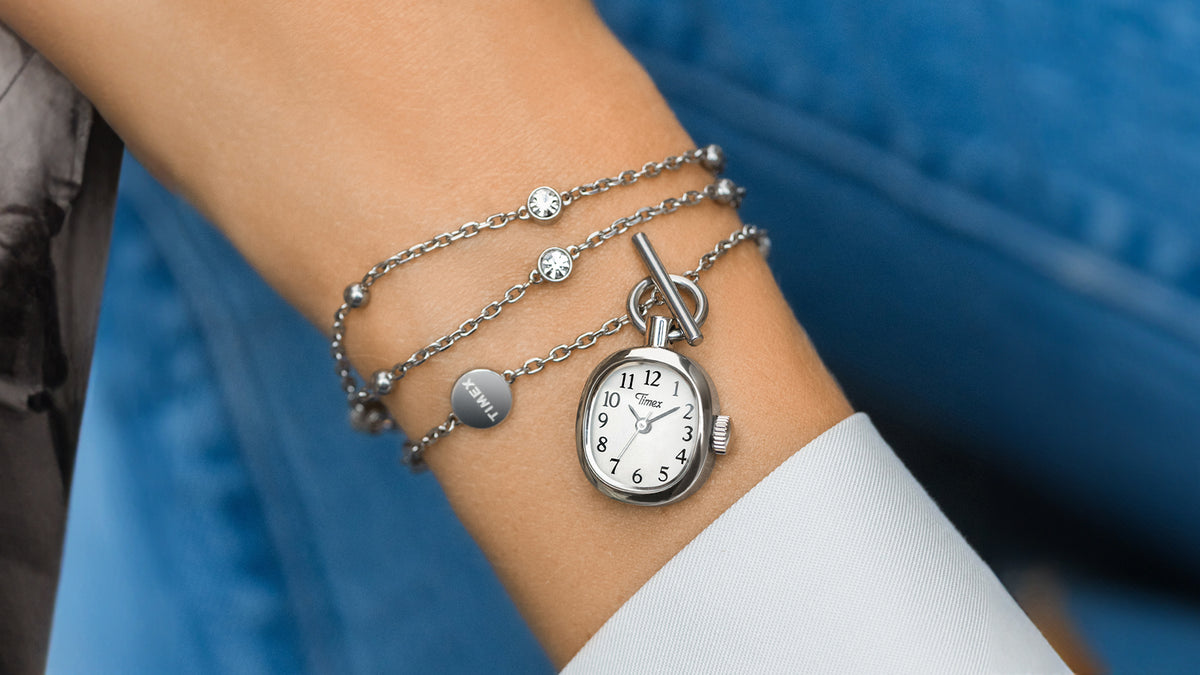 TW6A17600: collar Cavatina® Mini enrollado alrededor de una muñeca, en el que se aprecian el colgante en forma de reloj, el cierre de palanca y la cadena plateada con piedras transparentes.