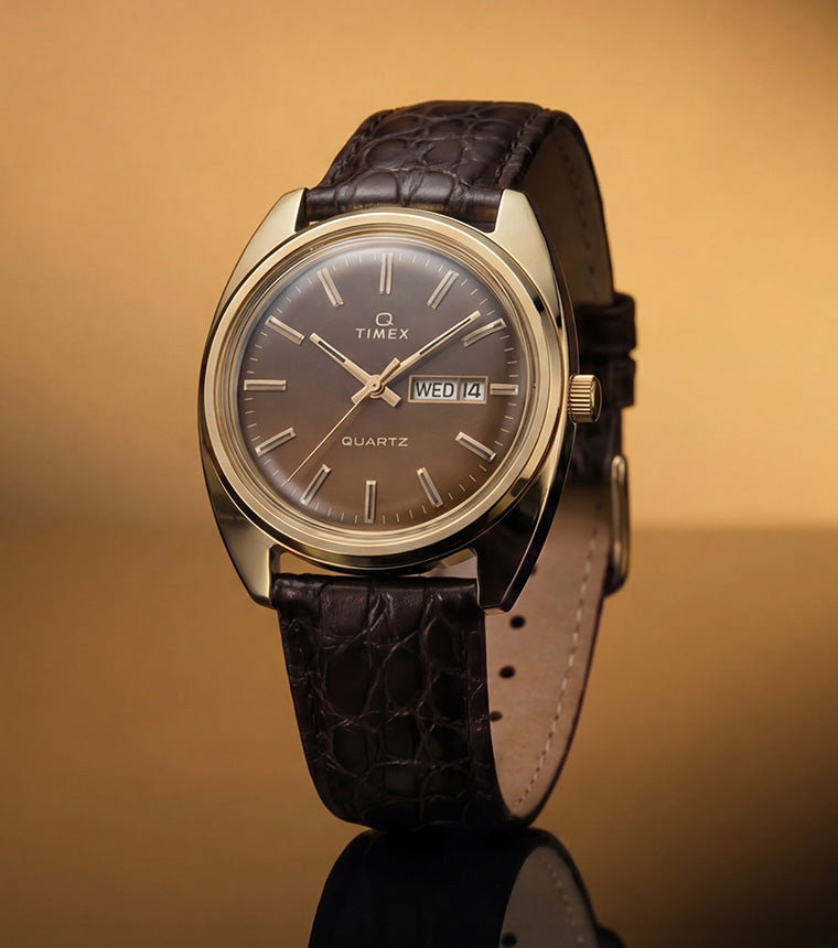 TW2Y87200 Timex 1978 Day Date Fumé Reissue with a gold-tone case, brown gradient dial, and textured brown leather strap against a warm gold background.