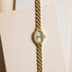 Reloj Timex Cavatina® Crystals TW2Y90200 con esfera ovalada con números romanos y bisel con cristales, colocado en posición vertical sobre papel color crema.