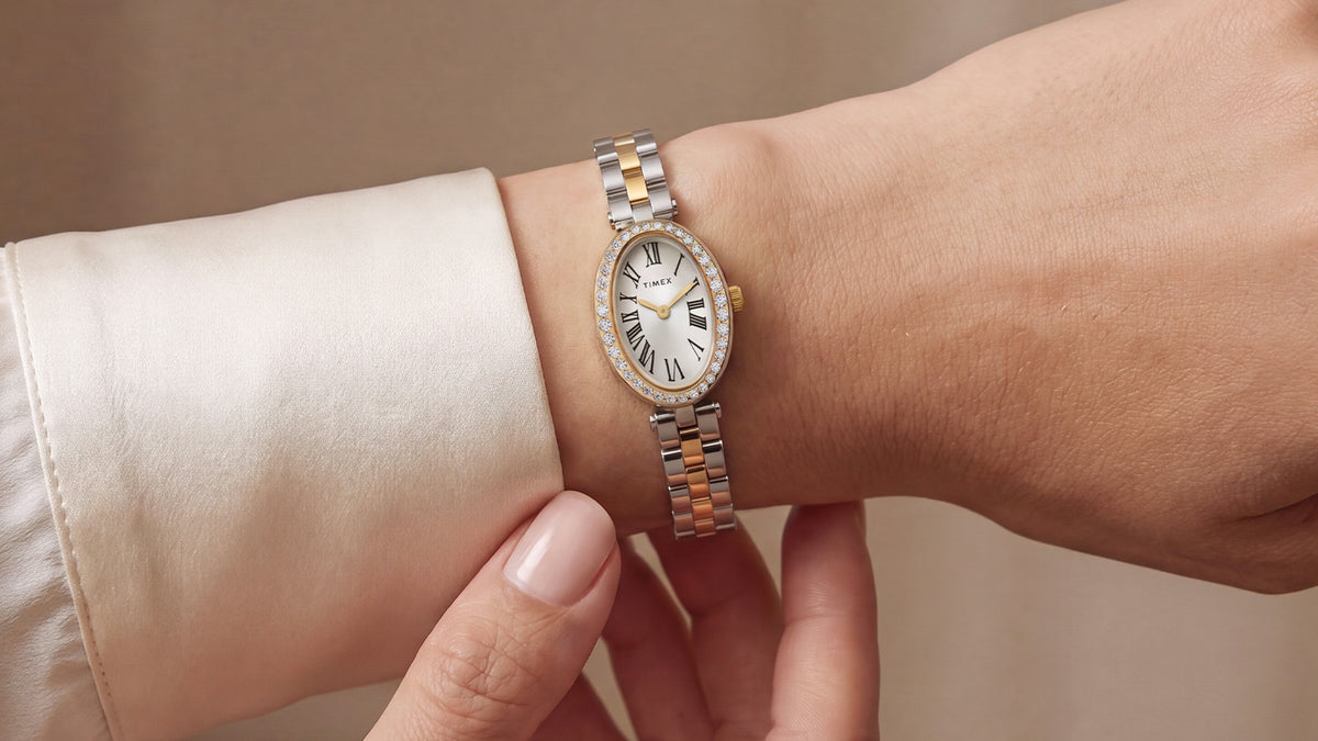 Reloj Timex Cavatina® Crystals (TW2Y90200) en una muñeca, en el que se aprecia su delgada pulsera bicolor y su caja con cristales incrustados junto a un puño de color marfil.