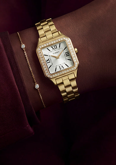 TW2Y90500 Gold-tone Timex Addison watch with a crystal-lined bezel and white Roman numeral dial, styled with a delicate bracelet and burgundy outfit.