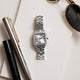 TW2Y90300 Silver-tone Timex Addison watch with a rectangular white dial and crystal-lined bezel, arranged on paper beside a pen and sunglasses.